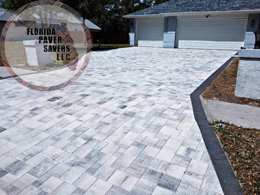 Light gray paver driveway with a dark border leading to a white garage