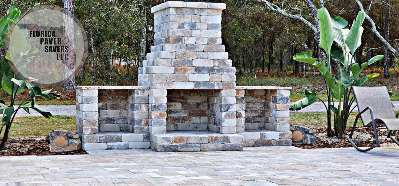 Outdoor stone fireplace with a tall chimney and side hearths on a paver patio