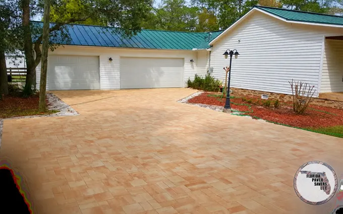 Sweeping tan paver driveway in front of a white detached garage
