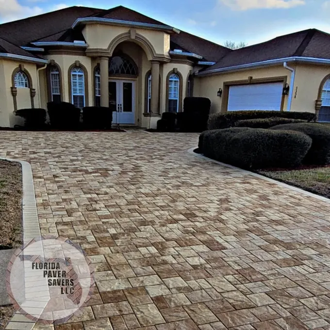 Broad paver driveway in front of an arched entrance and garage