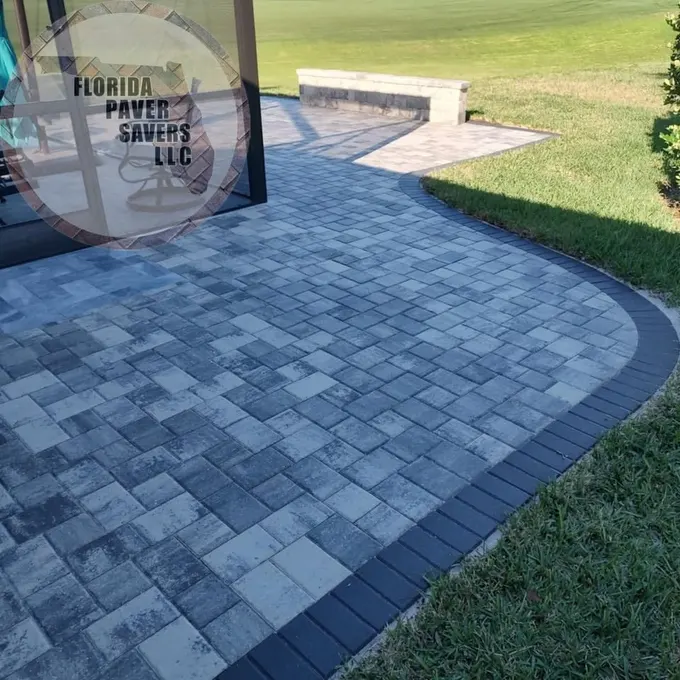 Curved gray paver patio with a dark border beside a lawn