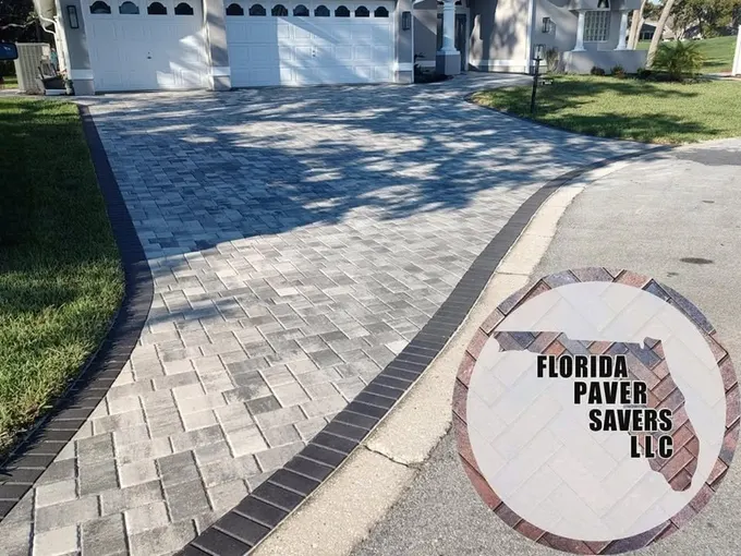 Gray paver driveway with a curved dark border approaching a white garage