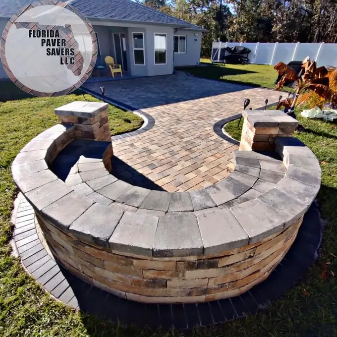 Curved stone seating wall with capped pillars beside a backyard paver patio