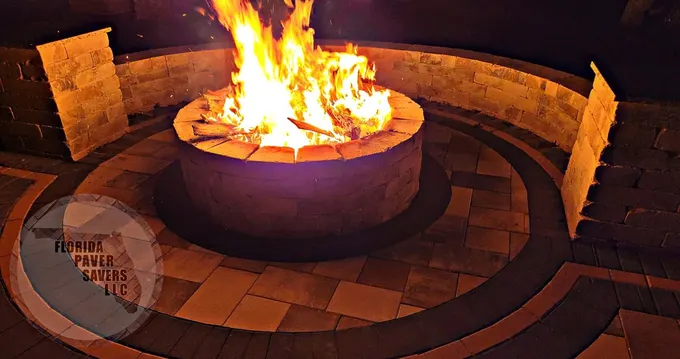 Round backyard fire pit burning at night beside a curved seating wall