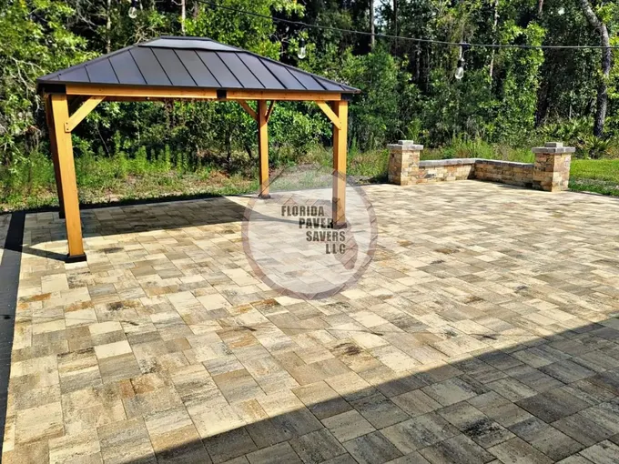 Large tan paver patio with a wooden gazebo and low stone walls