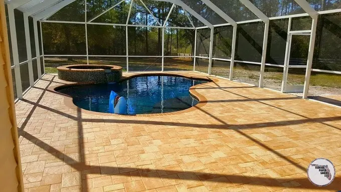 Warm tan paver pool deck around a swimming pool and raised spa inside a screen enclosure